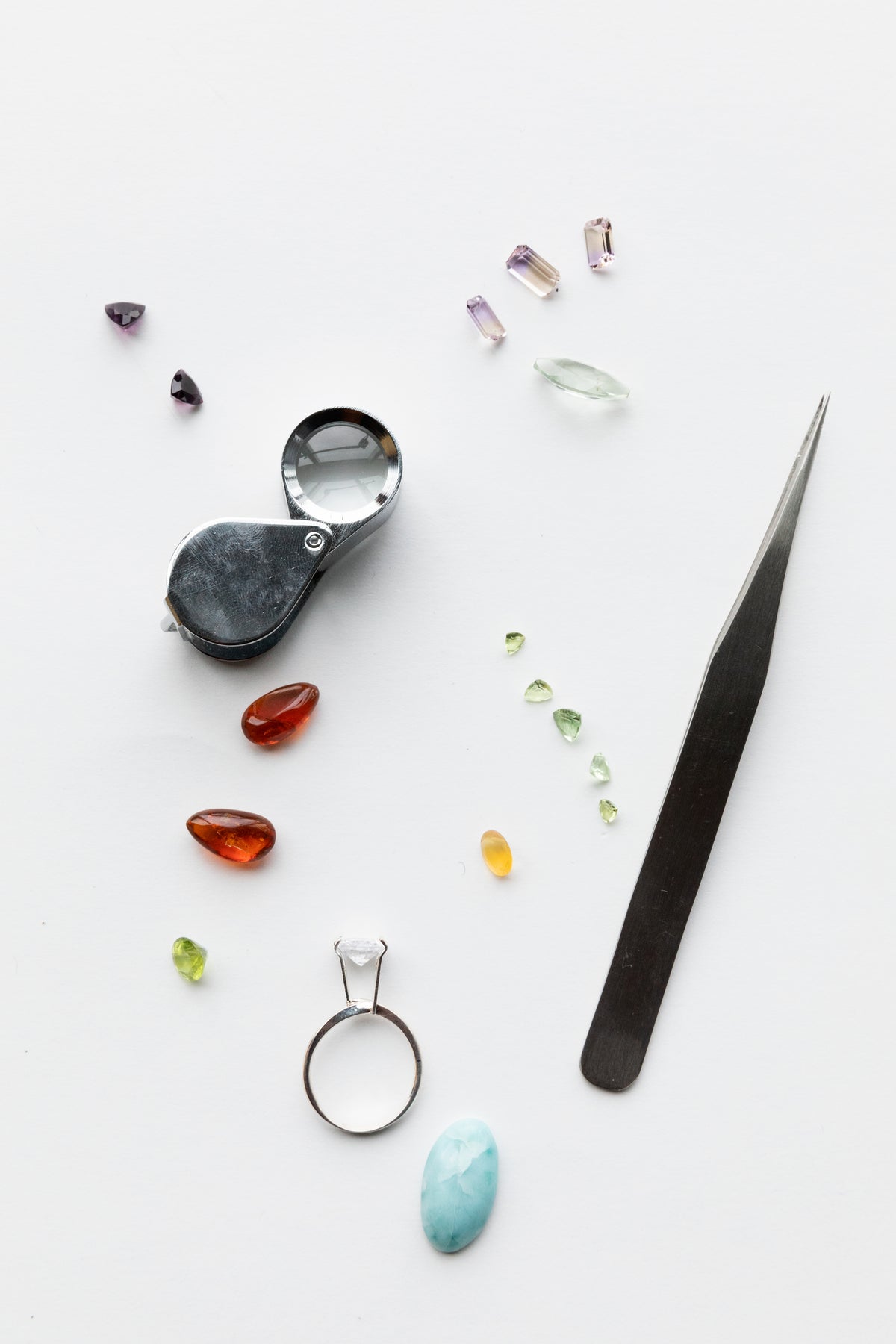Loose gemstones arranged beside a jeweller’s loupe and tweezers